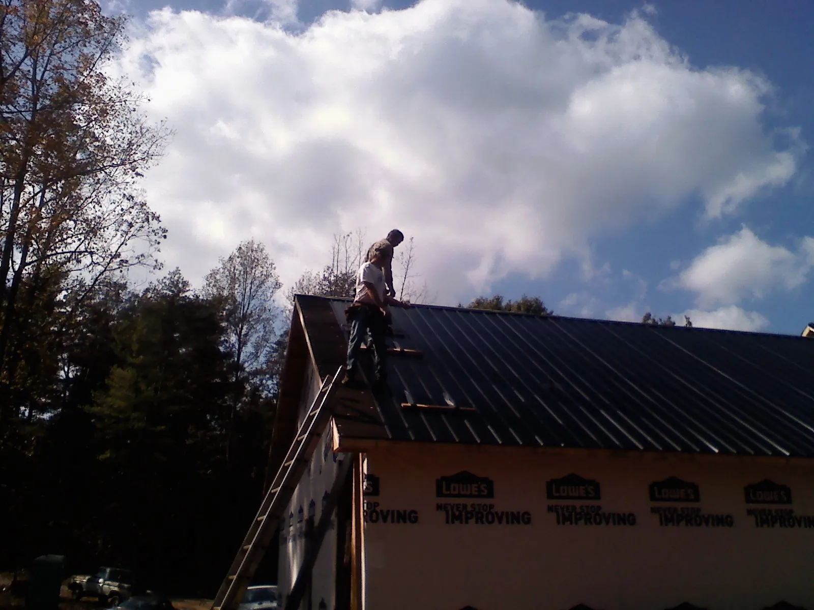 Roofer fastening dark metal panels high against a cloudy sky, from a Roof Inspection job in Boonsboro