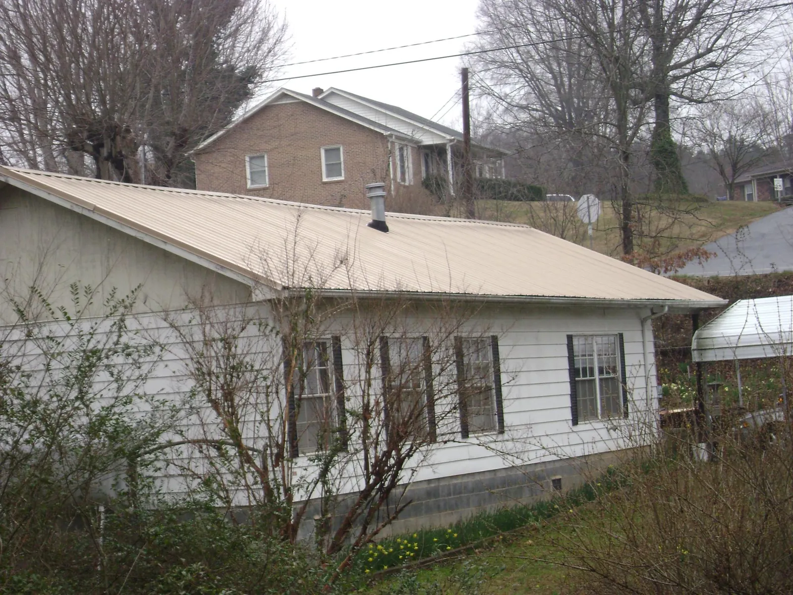 Tan metal roof on a white sided house set into a hillside — Commercial Roofing by Roofing Brothers in Boonsboro